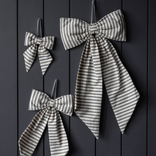 Load image into Gallery viewer, Three striped fabric bow decorations in different sizes hanging against a dark vertical wood plank background.