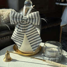 Load image into Gallery viewer, A clear glass bottle with a large gray-and-white striped bow, displayed on a white tablecloth in a sunlit living room setting. A brass candlestick and a small clear glass cup sit beside it.