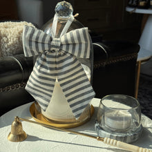 Load image into Gallery viewer, A clear glass bottle with a large gray-and-white striped bow, displayed on a white tablecloth in a sunlit living room setting. A brass candlestick and a small clear glass cup sit beside it.