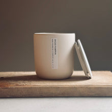 Load image into Gallery viewer, A matte ceramic candle jar with a matching lid resting beside it on a rustic wooden board, set against a neutral gray background.