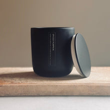 Load image into Gallery viewer, A matte black candle jar with its lid leaning against it on a wooden surface, set against a neutral beige background. The label reads 'SPICE ROOMS'.