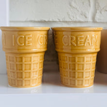 Load image into Gallery viewer, Two yellow ceramic ice cream cone-shaped canisters with embossed 'ICE CREAM' text, displayed on a white shelf against a white brick wall.
