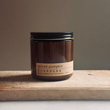 Load image into Gallery viewer, An amber glass jar candle with a black lid and a beige label reading 'spiced pumpkin' and 'ZCANDLES', placed on a rustic wooden board against a neutral background.
