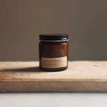 Load image into Gallery viewer, An amber glass jar candle with a black lid and a beige label reading 'spiced pumpkin' and 'SCANDIES', placed on a wooden board against a neutral background.
