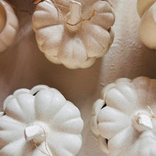 Load image into Gallery viewer, A close-up of several decorative ceramic pumpkins in a warm off-white, speckled finish, arranged on a textured beige surface.
