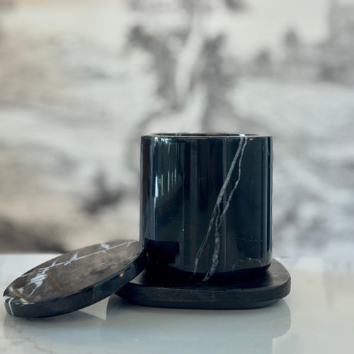 Black marble-patterned container with lid on a light surface, blurred floral background