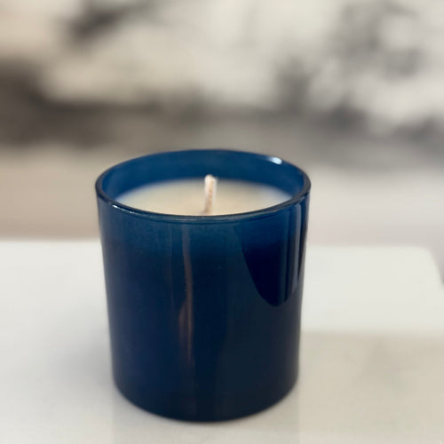 Blue candle in a glass container on a white surface with a blurred background