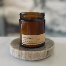 Load image into Gallery viewer, Candle jar labeled &#39;olive tree&#39; on a stone coaster with a blurred background
