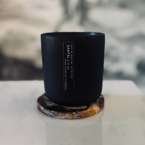 Black candle with a label on a white surface, blurred background