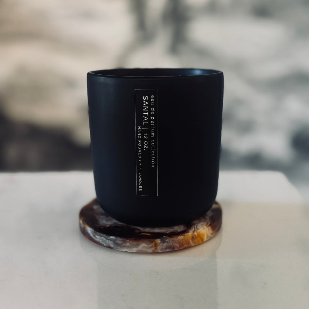 Black candle with a label on a white surface, blurred background