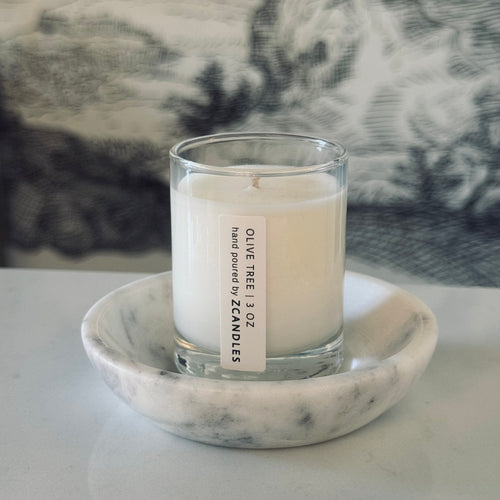 Candle in a glass holder on a marble coaster with a blurred background