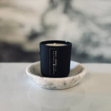 Load image into Gallery viewer, Black candle in a marble dish with a blurred background
