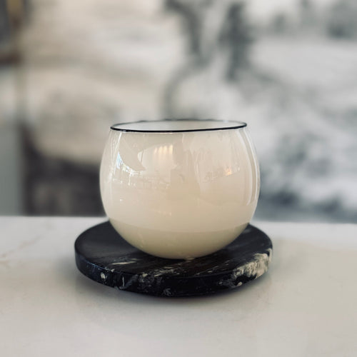 White glass candle holder on a black marble coaster with a blurred background