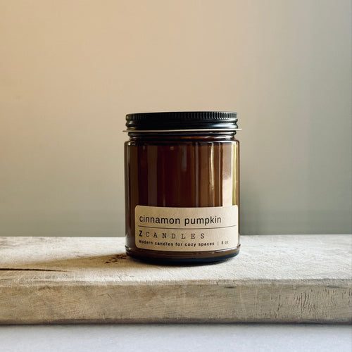 Candle jar labeled 'cinnamon pumpkin' on a wooden surface with a neutral background
