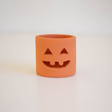 Load image into Gallery viewer, An orange terracotta ring-shaped candle holder with a carved jack-o'-lantern face, set against a plain white background.
